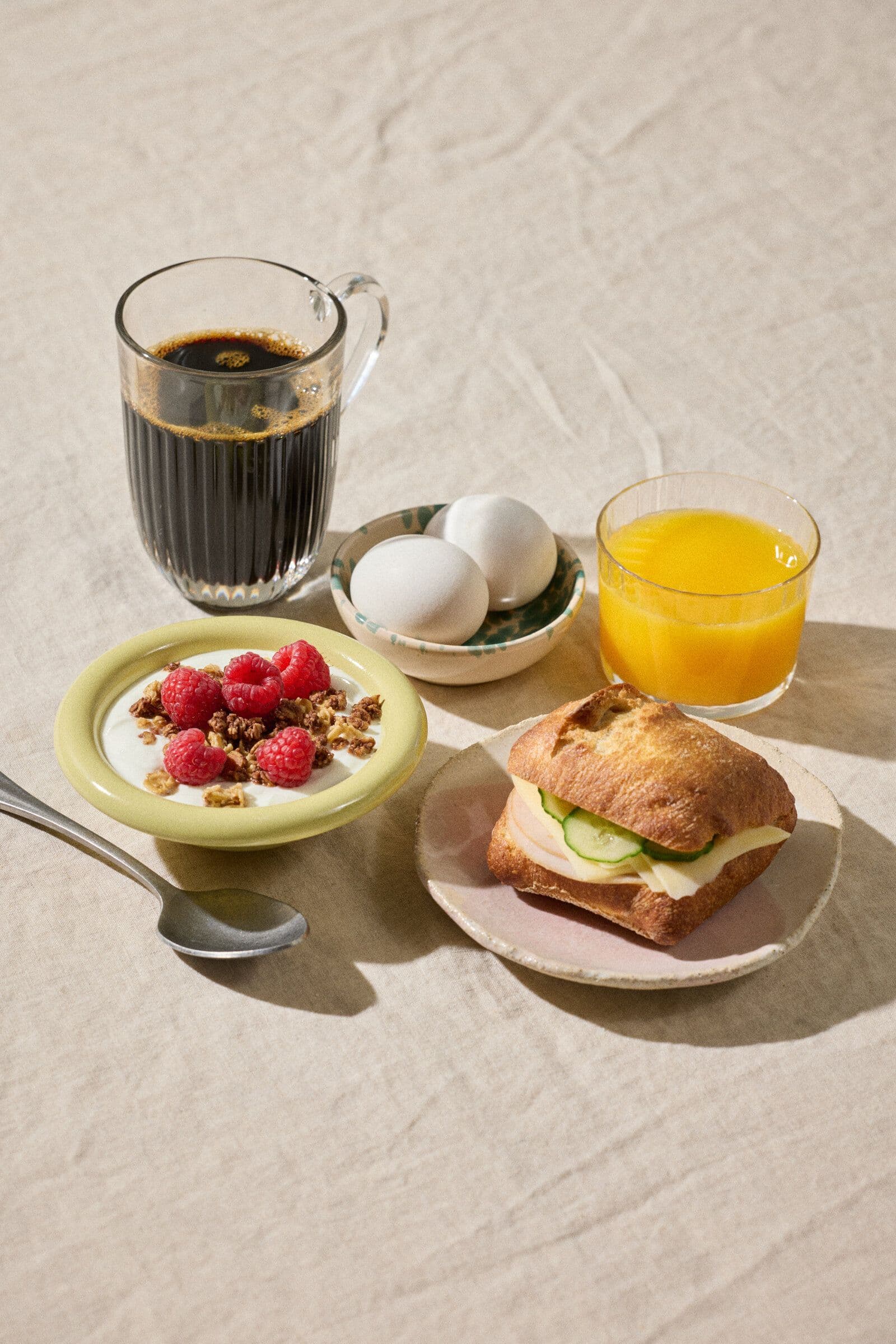 Frokost med yoghurt, bær, egg, sandwich og kaffe på bordet.